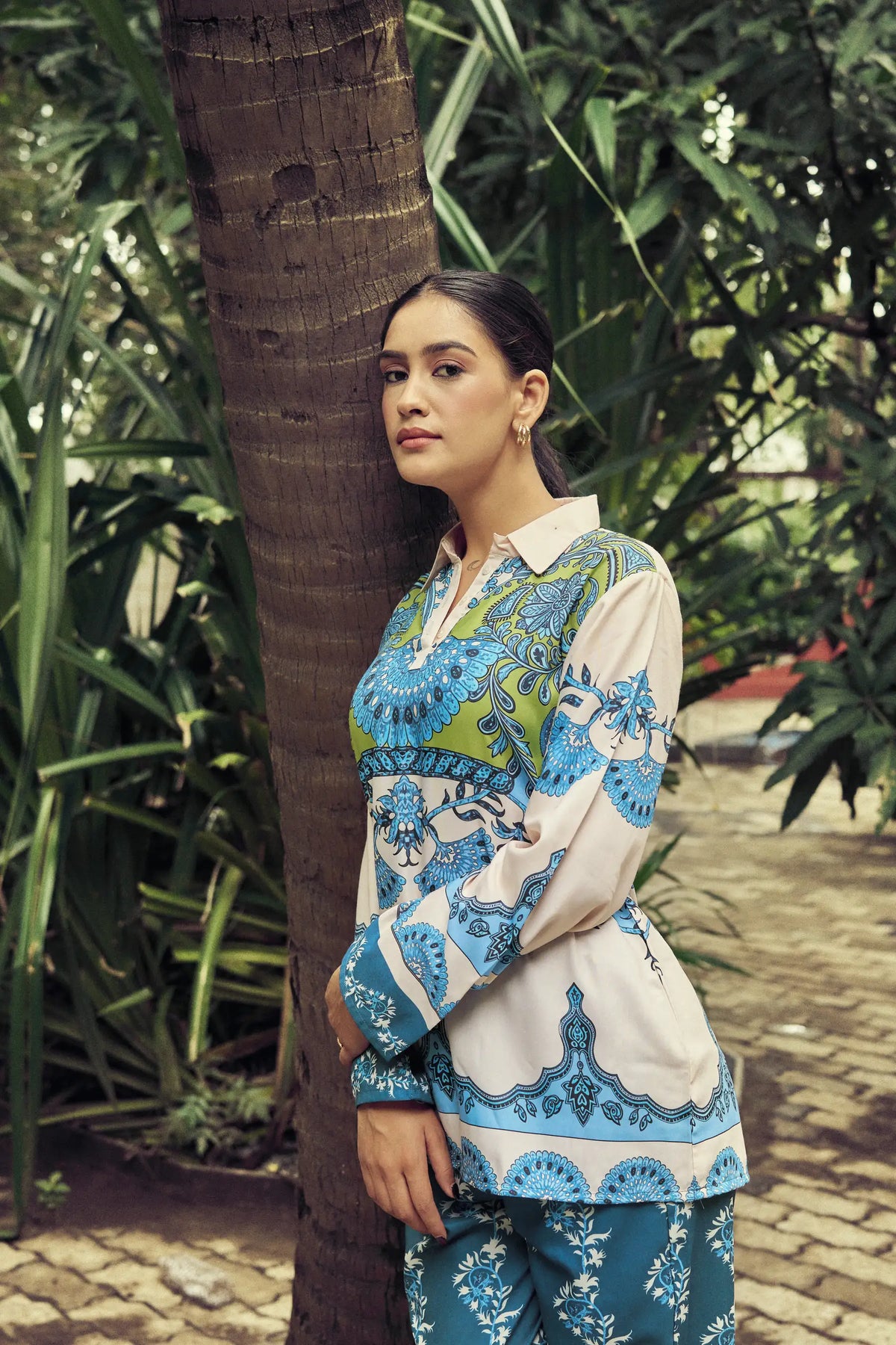 Model in a blue and ivory printed set beside a tree