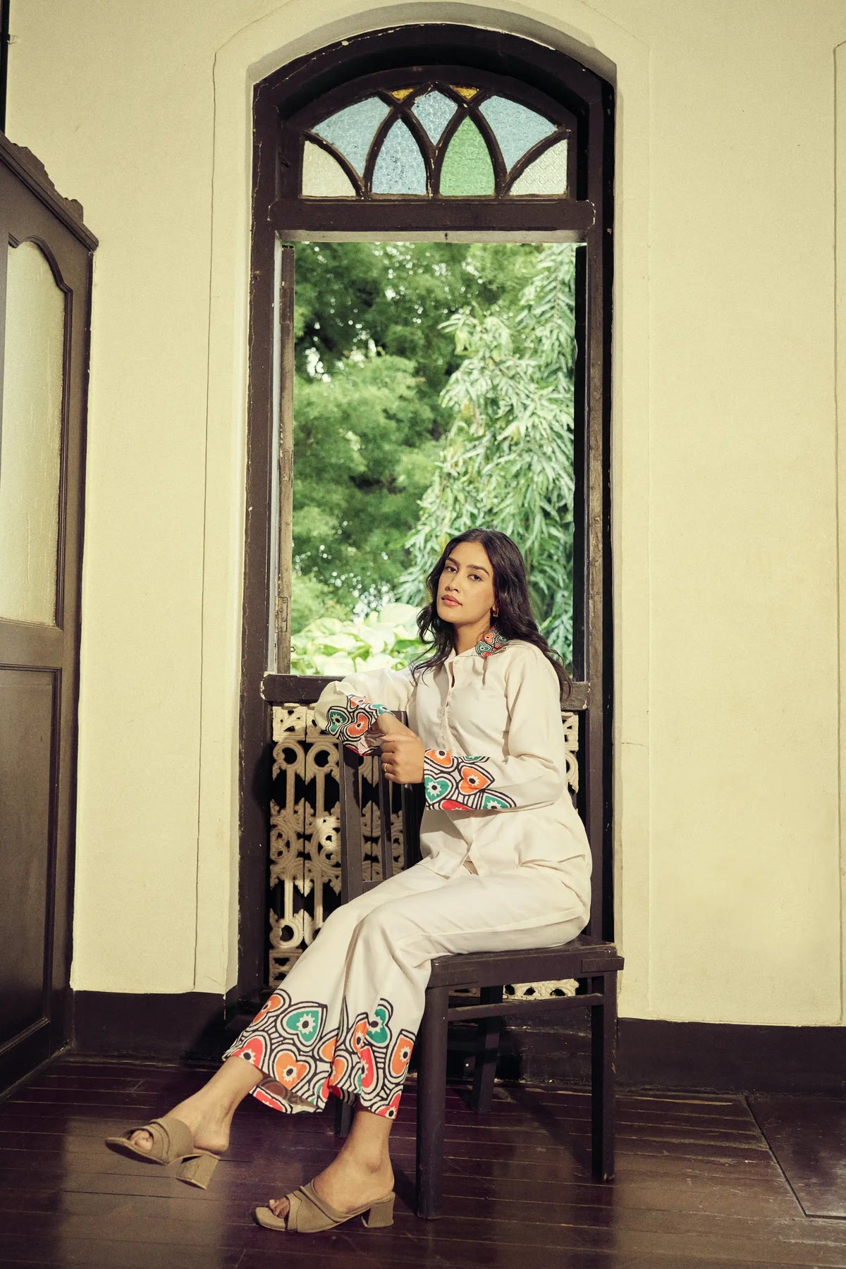 Model seated beside an arched window in a cream co-ord set